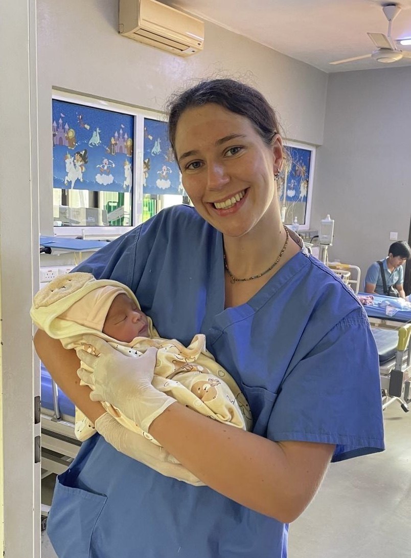 Eliza in medical scrubs holding a newborn baby.