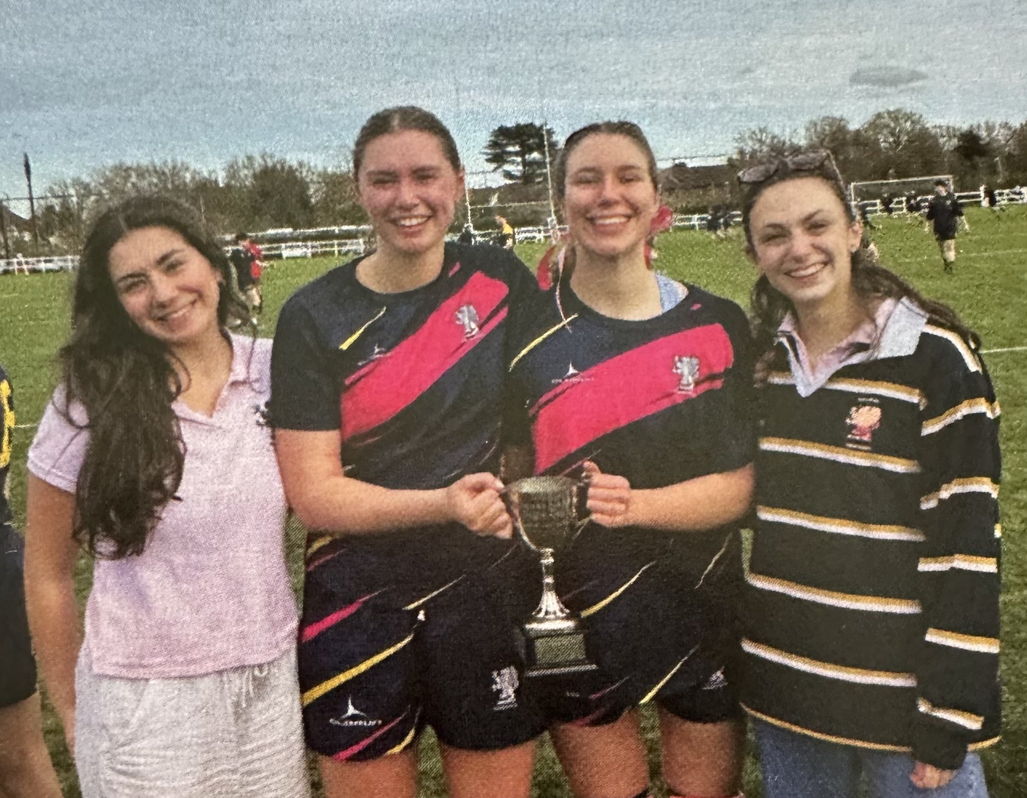 Friends with Eliza holding a trophy on a rugby field.