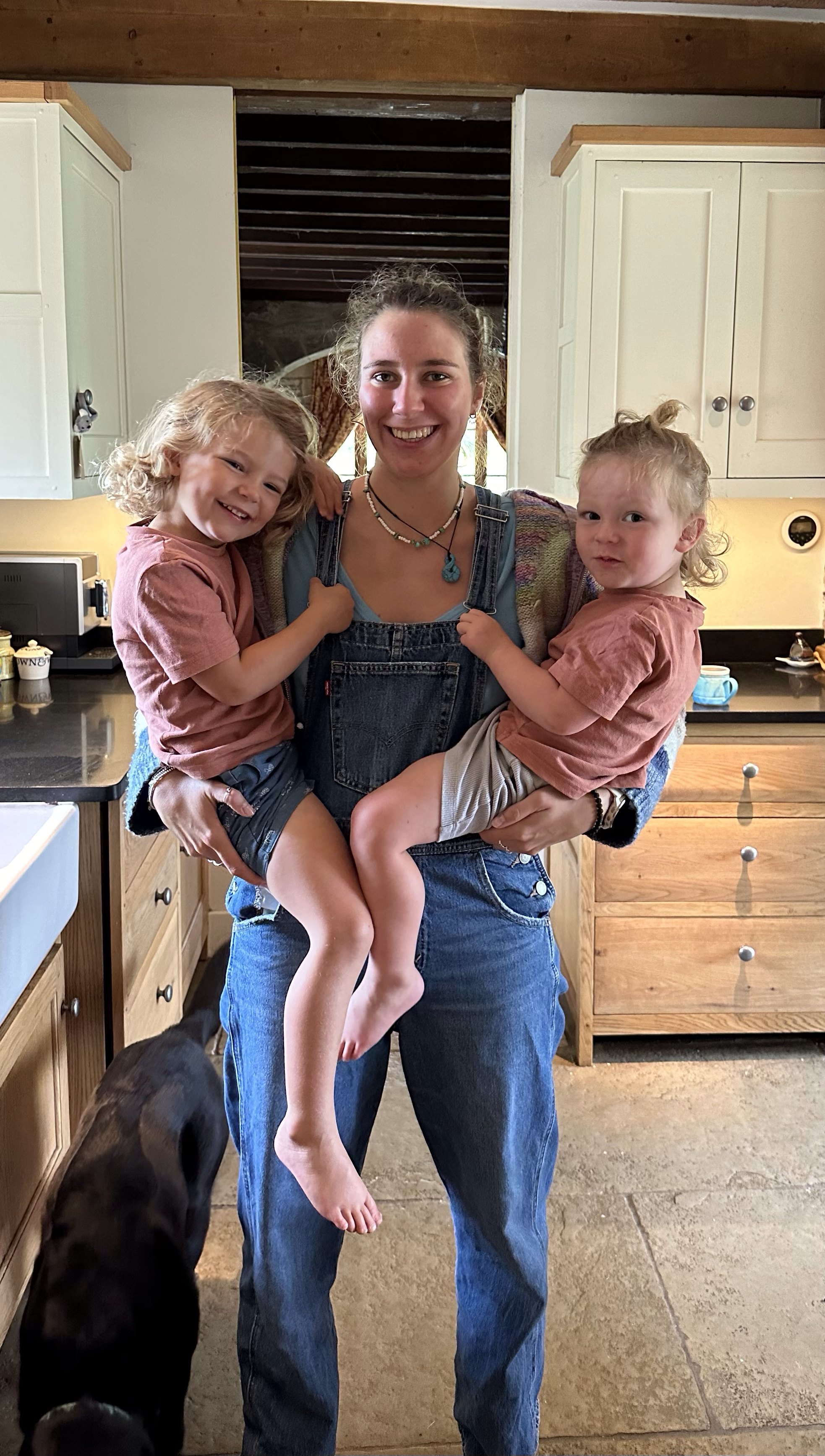 Eliza holding two children in a kitchen.